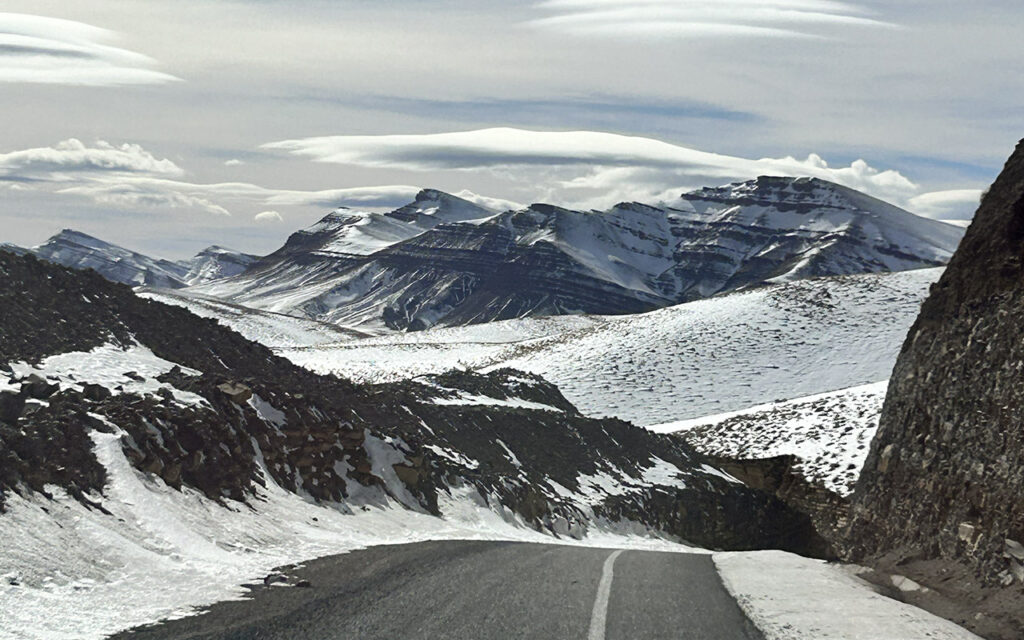 Long winding asphalt road through the rugged Atlas Mountains in Morocco under a clear blue sky.