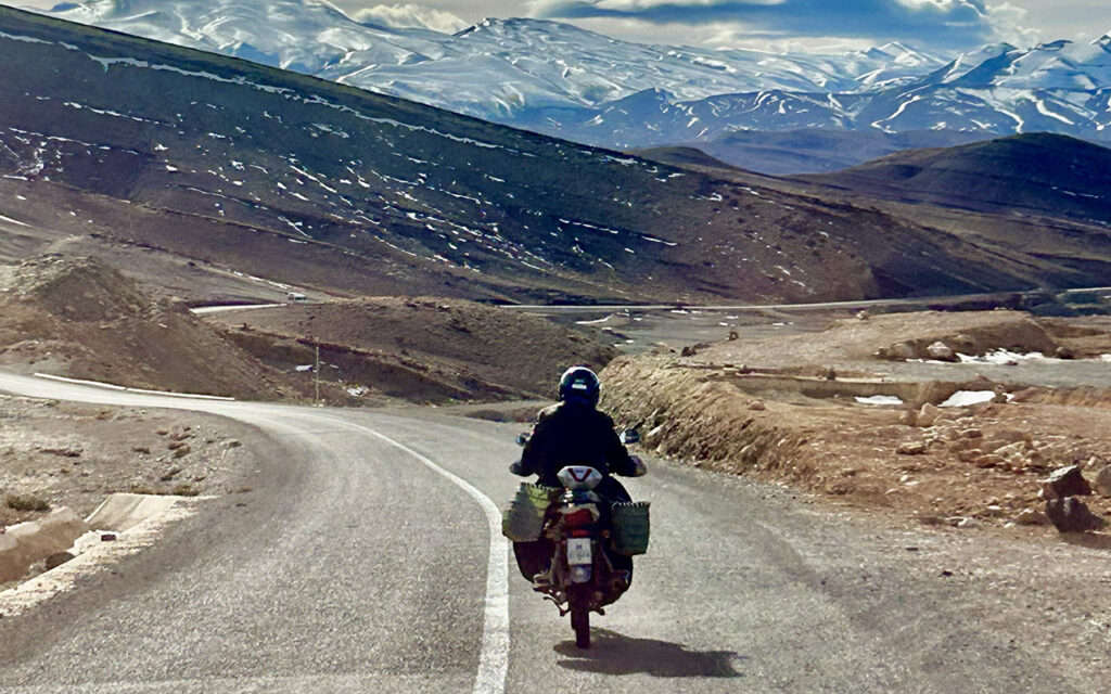Long winding asphalt road through the rugged Atlas Mountains in Morocco under a clear blue sky.