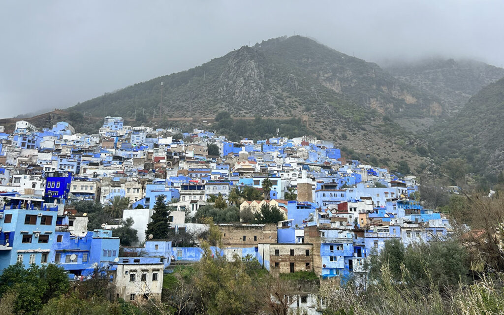 Panoramic view of the blue-washed city of Chefchaouen nestled in the green Rif Mountains of Morocco.