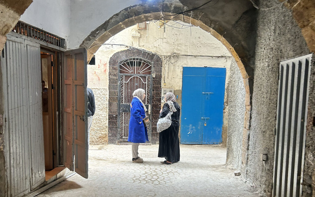 Two local women in traditional clothing having a conversation in a narrow street of a Moroccan Medina.