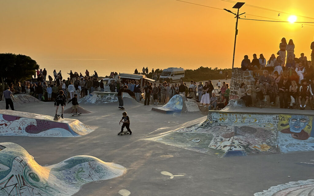 Large crowd gathered at Taghazout skatepark watching skaters during sunset, Morocco