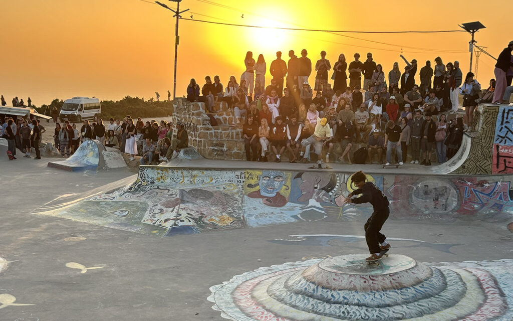 Large crowd gathered at Taghazout skatepark watching skaters during sunset, Morocco