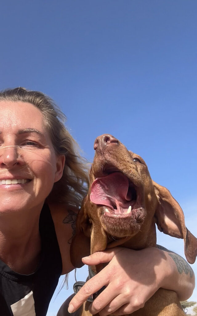A happy selfie of a woman and her yawning Vizsla dog under the blue Moroccan sky